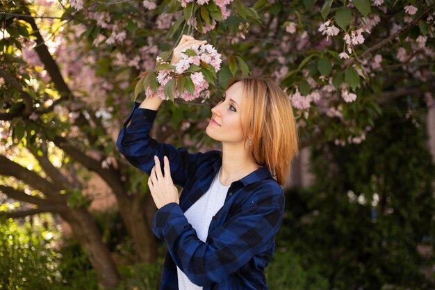 Hipster woman near sakura blooming tree Pink flowers spring and youth concept Stylish girl smiling