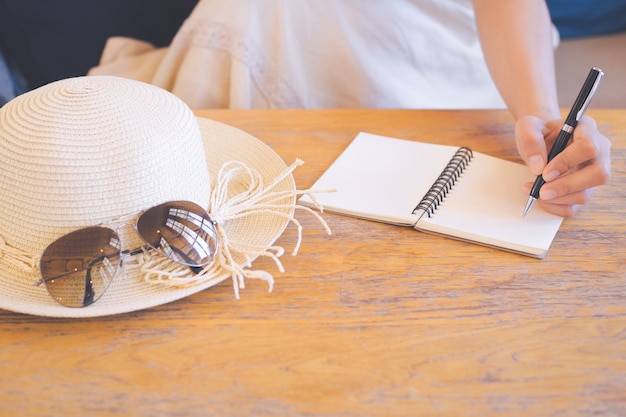 Hipster women hand in cream dresses are writing on notepad with a pen.