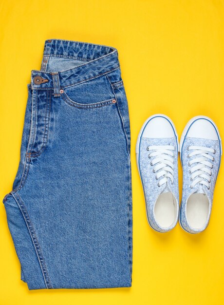 Hipster women sneakers with blue jeans on a yellow background. top view, flat lay, minimalism