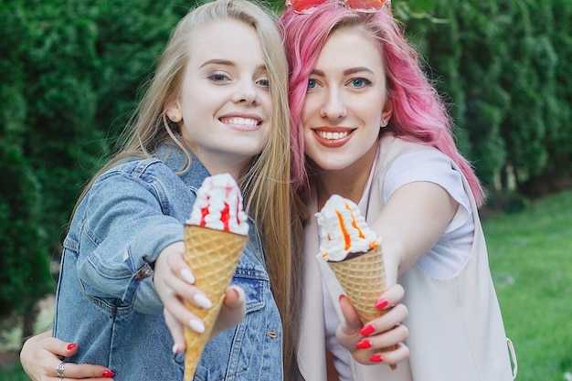 Hipster young adult friends embracing while hanging out in the city. Two young women laughing and walking enjoying carefree vacation lifestyle. Two pretty girlfriends eating ice cream in the city