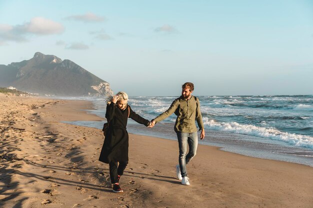 Hipster young couple in love walking together at sunset along the desert beach during the autumn season Love and youth concept