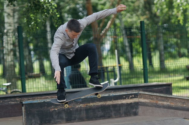 Hipster - giovane ragazzo carino in jeans e maglietta che fa skateboard sulle siepi nel soleggiato parco estivo