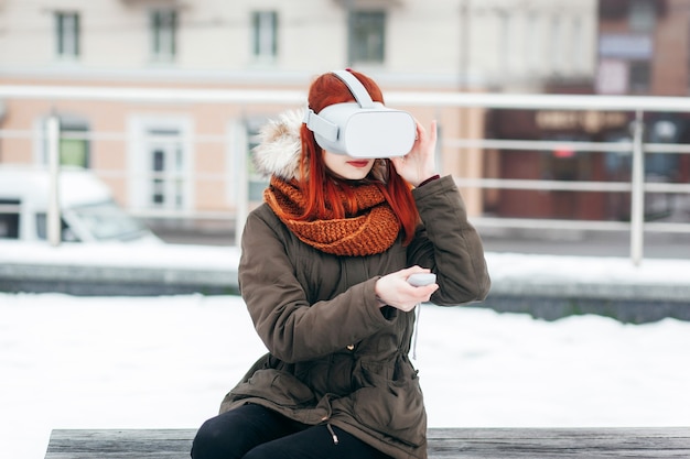 Hipster young girl plays virtual reality mobile game app on smartphone attached to modern VR glasses outdoor