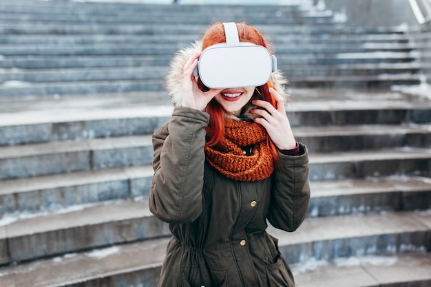 Hipster 어린 소녀가 현대 VR 안경에 연결된 스마트 폰에서 가상 현실 모바일 게임 앱을 재생합니다.