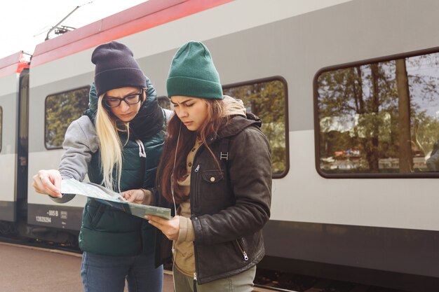 バックパックと地図を持つ流行に敏感な若い女の子は、電車を待ちます。