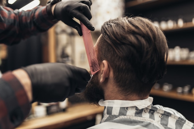 Hipster young good looking man visiting barber shop. Trendy and stylish beard styling and cut.