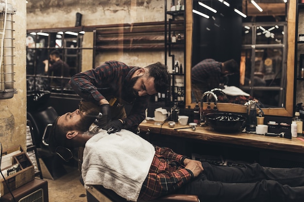 Hipster young good looking man visiting barber shop. Trendy and stylish beard styling and cut.