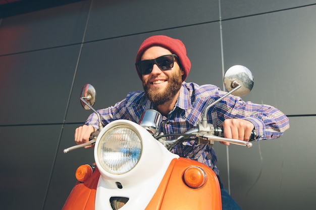 Hipster young  man in helmet is riding on yellow retro scooter in town