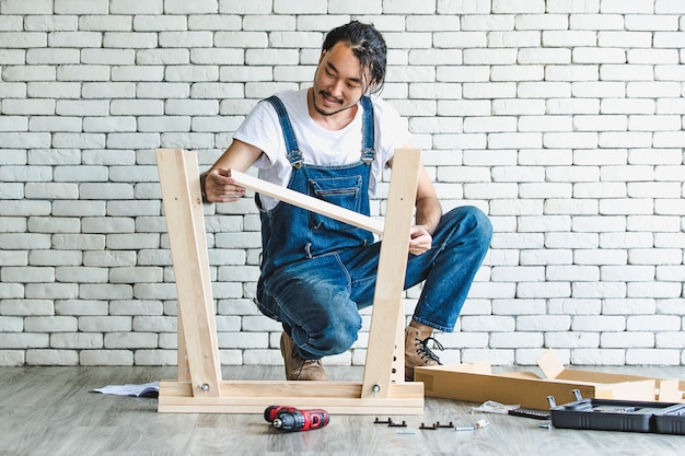 Hipster young man working as handyman, assembling wood table with equipments