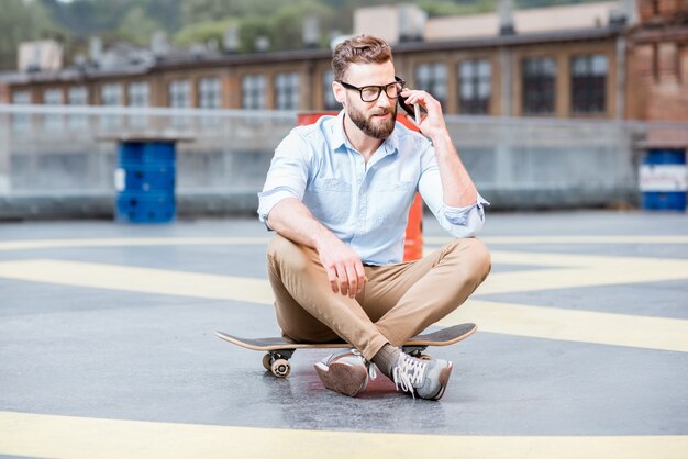 Hipster zakenman praten met slimme telefoon op de speelplaats op het dak van het industriële gebouw. Lifestyle bedrijfsconcept