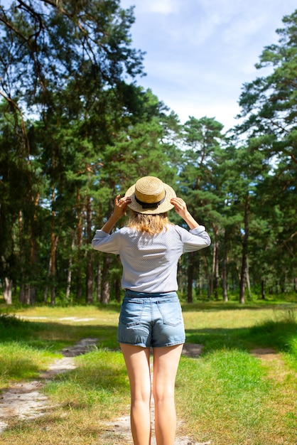 Hipstermeisje in strohoed die zich in het bos bevinden. Wanderlust-concept. Ideeën voor reizen. Mooie vrouw in de natuur. Zomerse sferen.