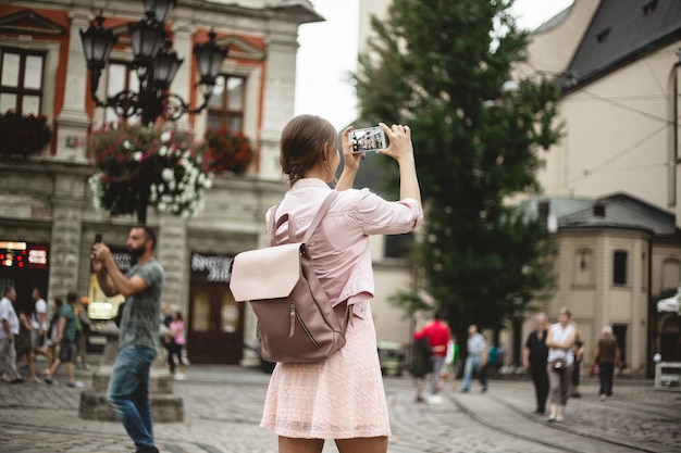 Hipstermeisje met rugzak houdt smartphone vast Reiziger fotografeert het stadsbeeld bij zonsondergang Lifestyle