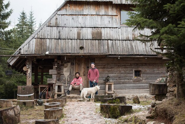 Foto ritratto di coppia hipsters, due giovani con cane husky bianco seduto davanti alla vecchia casa retrò in legno