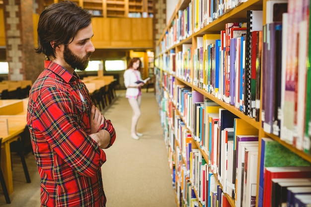 Hipsterstudent die een boek in bibliotheek plukt