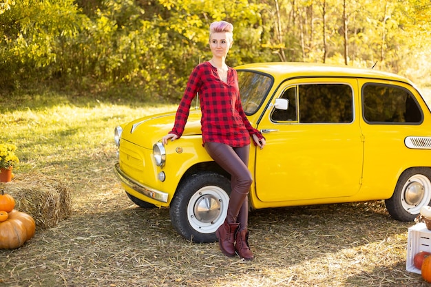 Hipstervrouw dichtbij gele retro auto op de achtergrond van het de herfstpark met gouden bomen