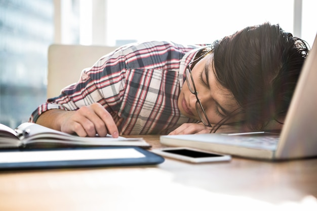 Hipsterzakenman die in slaap op bureau in bureau vallen