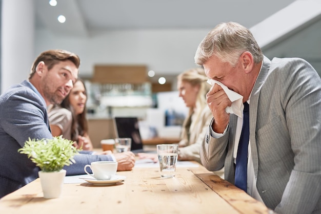 His allergies are drawing unwanted attention Cropped shot of a businessman blowing his nose while his colleagues look on in disgust