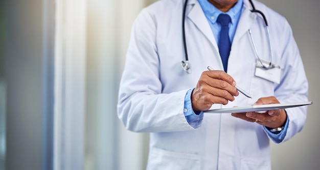 His schedules are always busy Shot of an unrecognizable male doctor writing on a digital tablet while standing inside of a hospital during the day