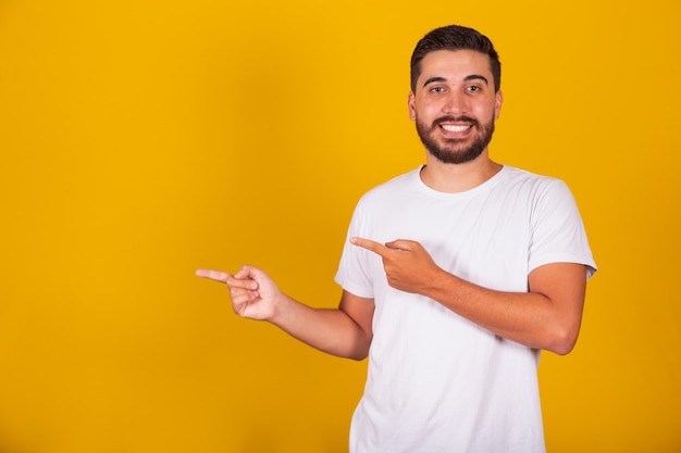 Hispanic brazilian man with arms hands and fingers pointed to the side for negative space advertising concept suggestion concept choice concept yellow background