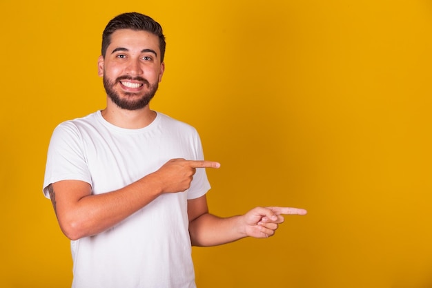 Hispanic Brazilian man with arms hands and fingers pointed to the side for negative space advertising concept suggestion concept choice concept yellow background