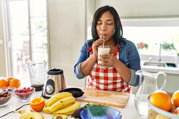 Hispanic brunette woman drinking fresh fruit smoothie at the kitchen