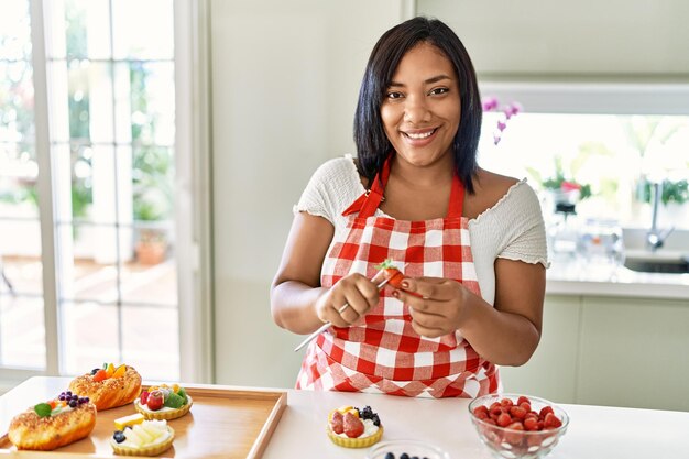 Hispanic brunette woman preparing pastries with strawberry at the kitchen