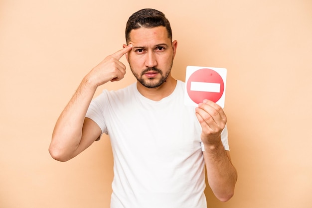 Hispanic caucasian man holding a forbidden sign isolated on beige background
