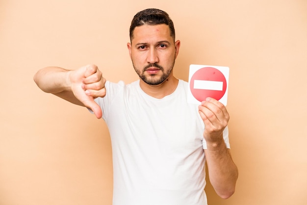 Hispanic caucasian man holding a forbidden sign isolated on beige background