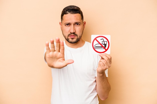 Hispanic caucasian man holding no eating sign isolated on beige background