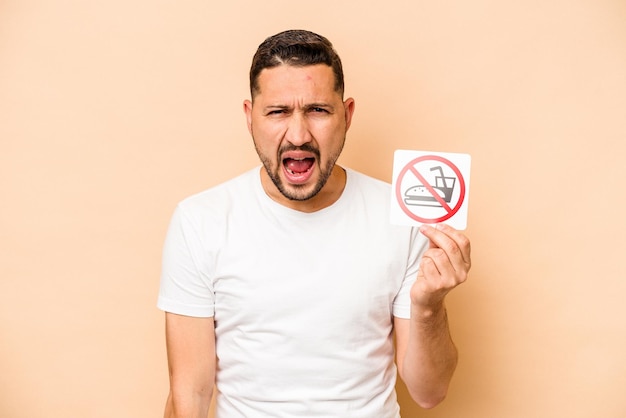 Hispanic caucasian man holding no eating sign isolated on beige background