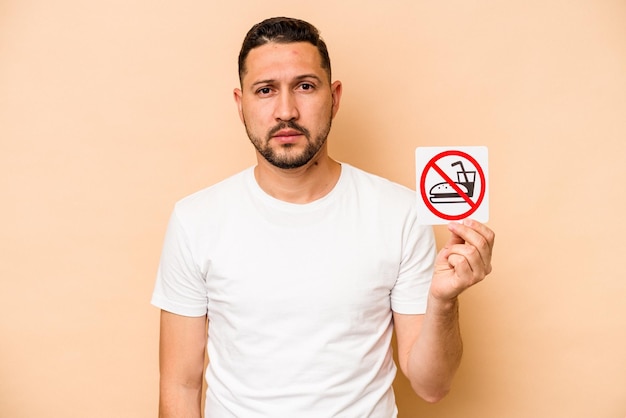 Hispanic caucasian man holding no eating sign isolated on beige background