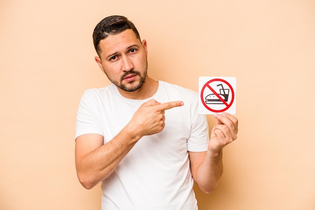 Photo hispanic caucasian man holding no eating sign isolated on beige background