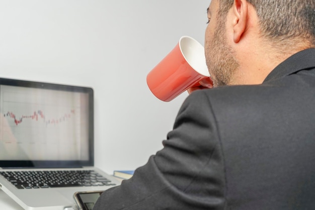 Hispanic executive calmly reviews his companys investments\
while sipping coffee in a red cup