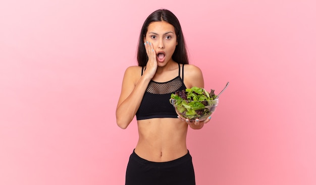 Hispanic fitness woman feeling shocked and scared and holding a salad