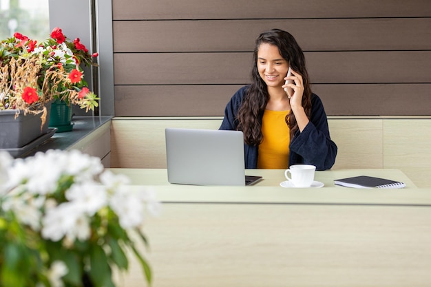 Hispanic freelancer using laptop and speaking on cellphone