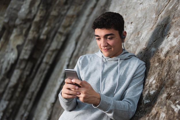 Hispanic generatie z jongen met behulp van mobiele telefoon buitenshuis tegen muur