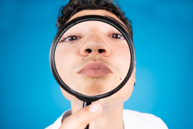 Hispanic guy kissing through loupe or magnifying glass isolated on blue background