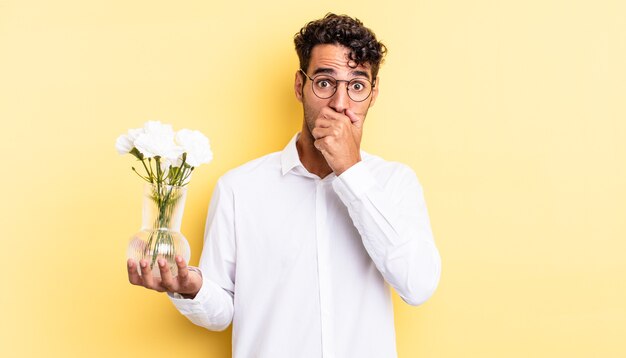 Bell'uomo ispanico che copre la bocca con le mani con uno scioccato. concetto di vaso di fiori