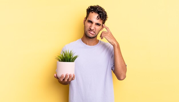 Hispanic handsome man feeling confused and puzzled, showing you are insane. decorative plant concept