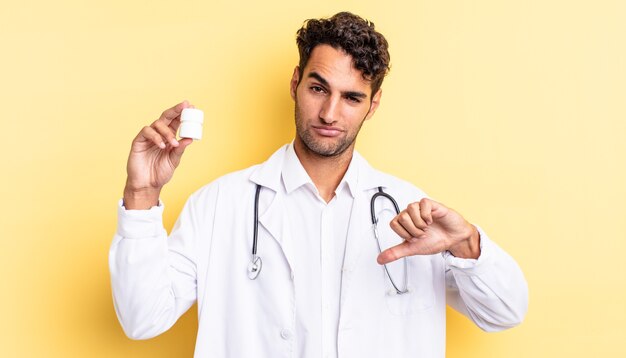 Hispanic handsome man feeling cross,showing thumbs down. physician bottle pills concept