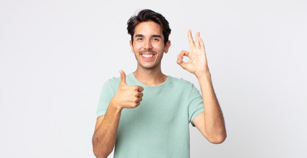 Hispanic handsome man feeling happy, amazed, satisfied and surprised, showing okay and thumbs up gestures, smiling