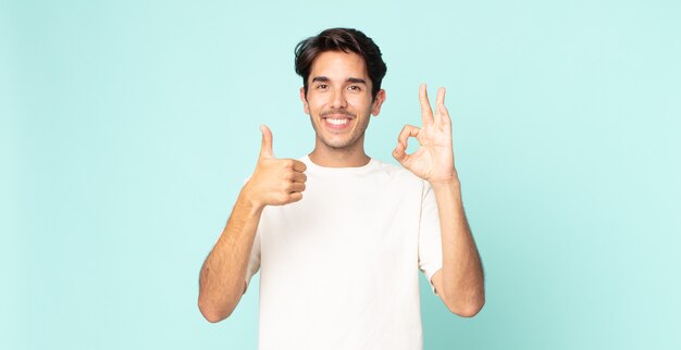 Hispanic handsome man feeling happy, amazed, satisfied and surprised, showing okay and thumbs up gestures, smiling