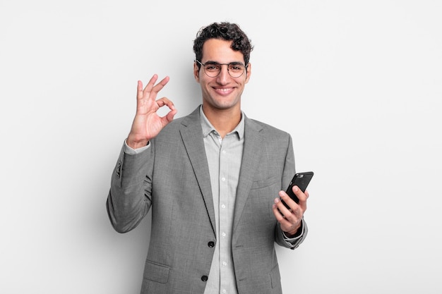 Hispanic handsome man feeling happy, showing approval with okay gesture. business and phone concept