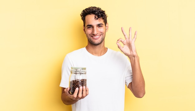 Hispanic handsome man feeling happy, showing approval with okay gesture. coffee beans bottle