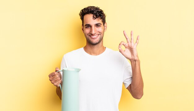 Hispanic handsome man feeling happy, showing approval with okay gesture. coffee thermos concept