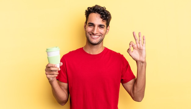 Hispanic handsome man feeling happy, showing approval with okay gesture. take away coffee concept