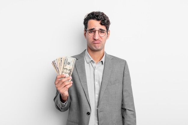 Hispanic handsome man feeling sad and whiney with an unhappy look and crying. business and dollar banknotes concept