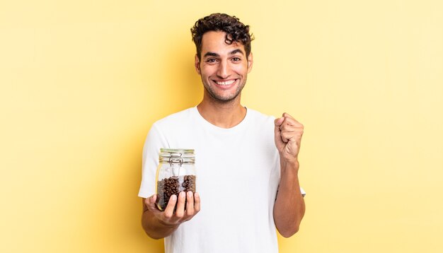 Hispanic handsome man feeling shocked,laughing and celebrating success. coffee beans bottle