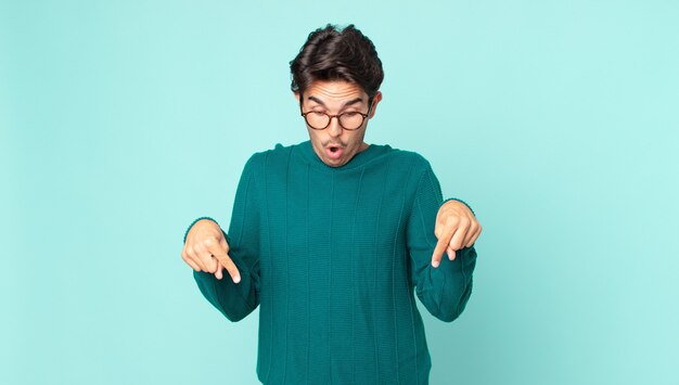 写真 ヒスパニック系のハンサムな男は、ショックを受け、口を開けて驚いて、不信と驚きで下を向いて見ています