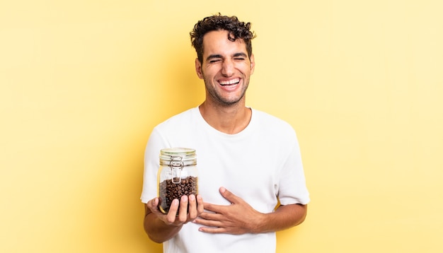 Hispanic handsome man laughing out loud at some hilarious joke. coffee beans bottle